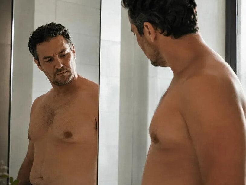 Man examining his chest in a mirror while researching male breast reduction in San Antonio