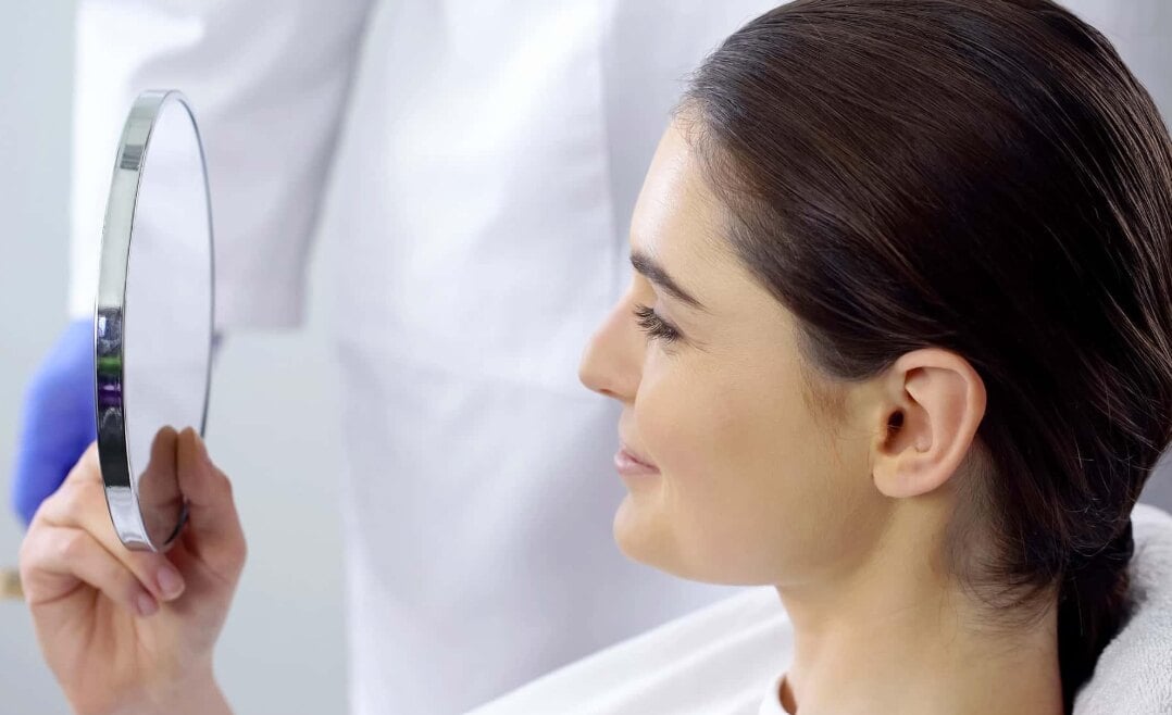 Patient reviewing her profile in a hand mirror after revision rhinoplasty in San Antonio