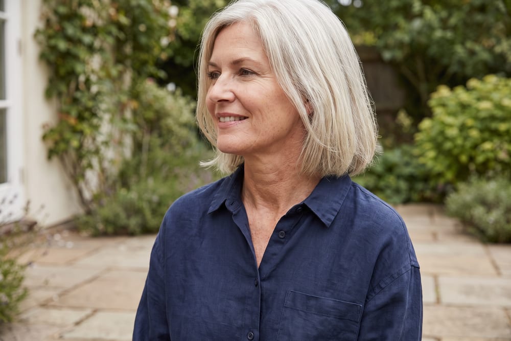 Woman in her fifties with silver-blonde hair turned in profile on a garden patio, her jawline and neck in view, illustrating the types of facelift in San Antonio